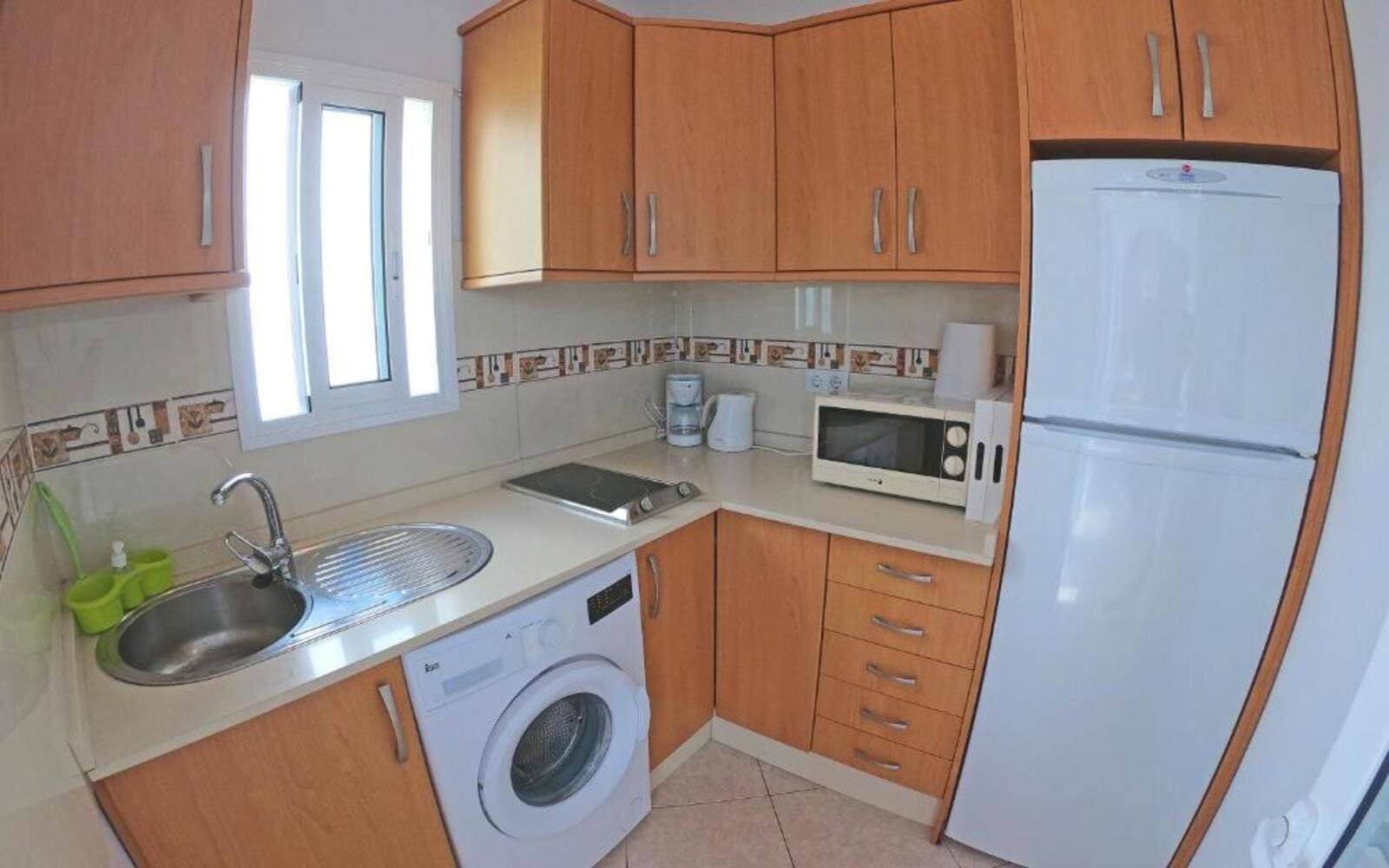 Una cocina con gabinetes de madera, lavadora y secadora, microondas y refrigerador.