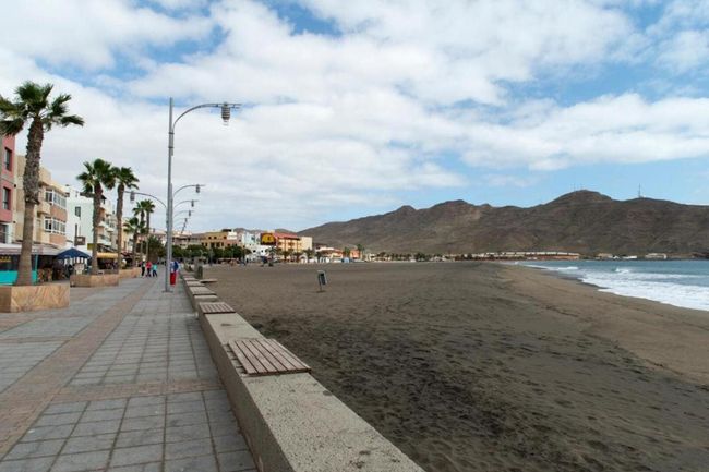 Una pasarela que conduce a una playa con montañas al fondo.