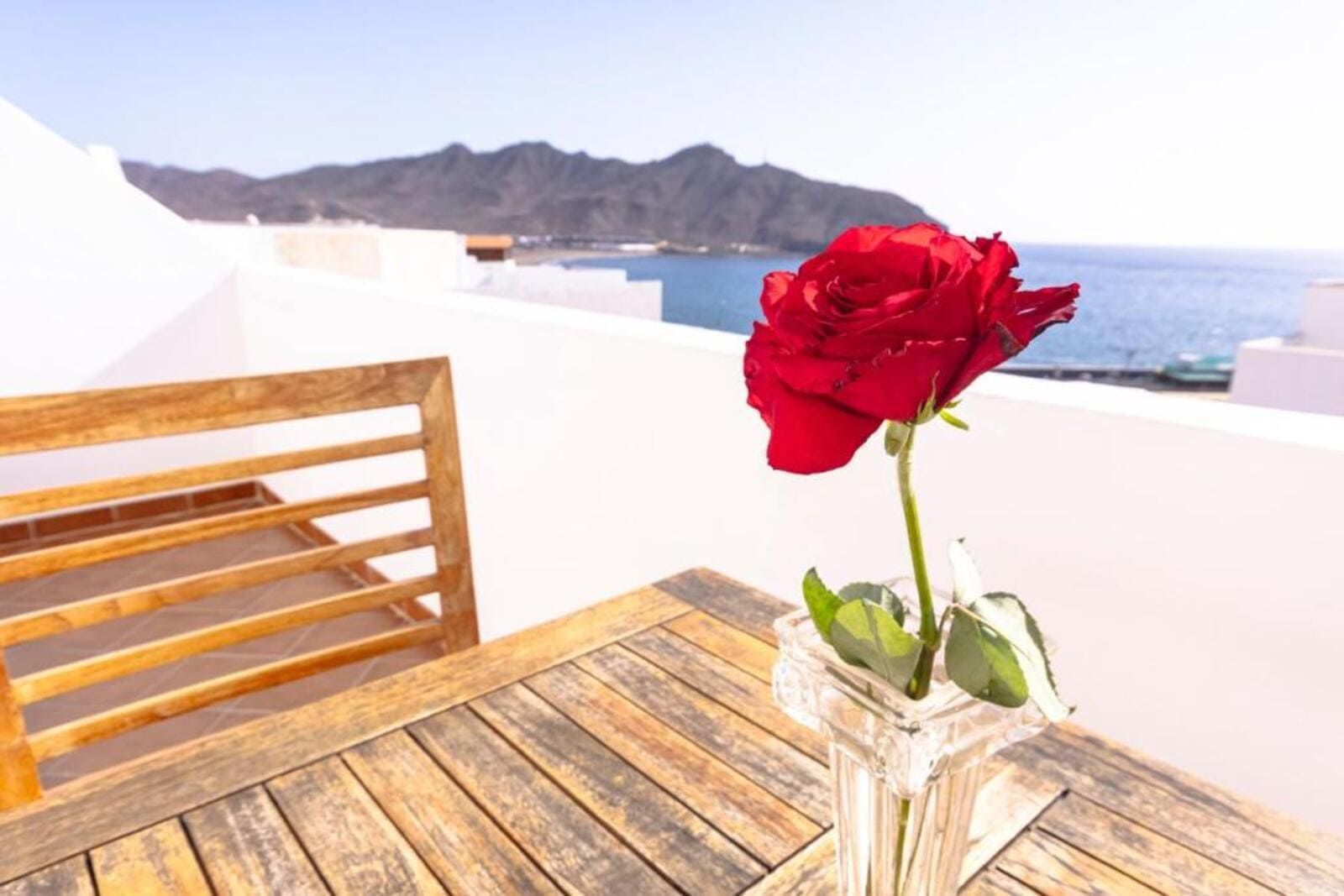 Una rosa roja está en un jarrón sobre una mesa de madera.