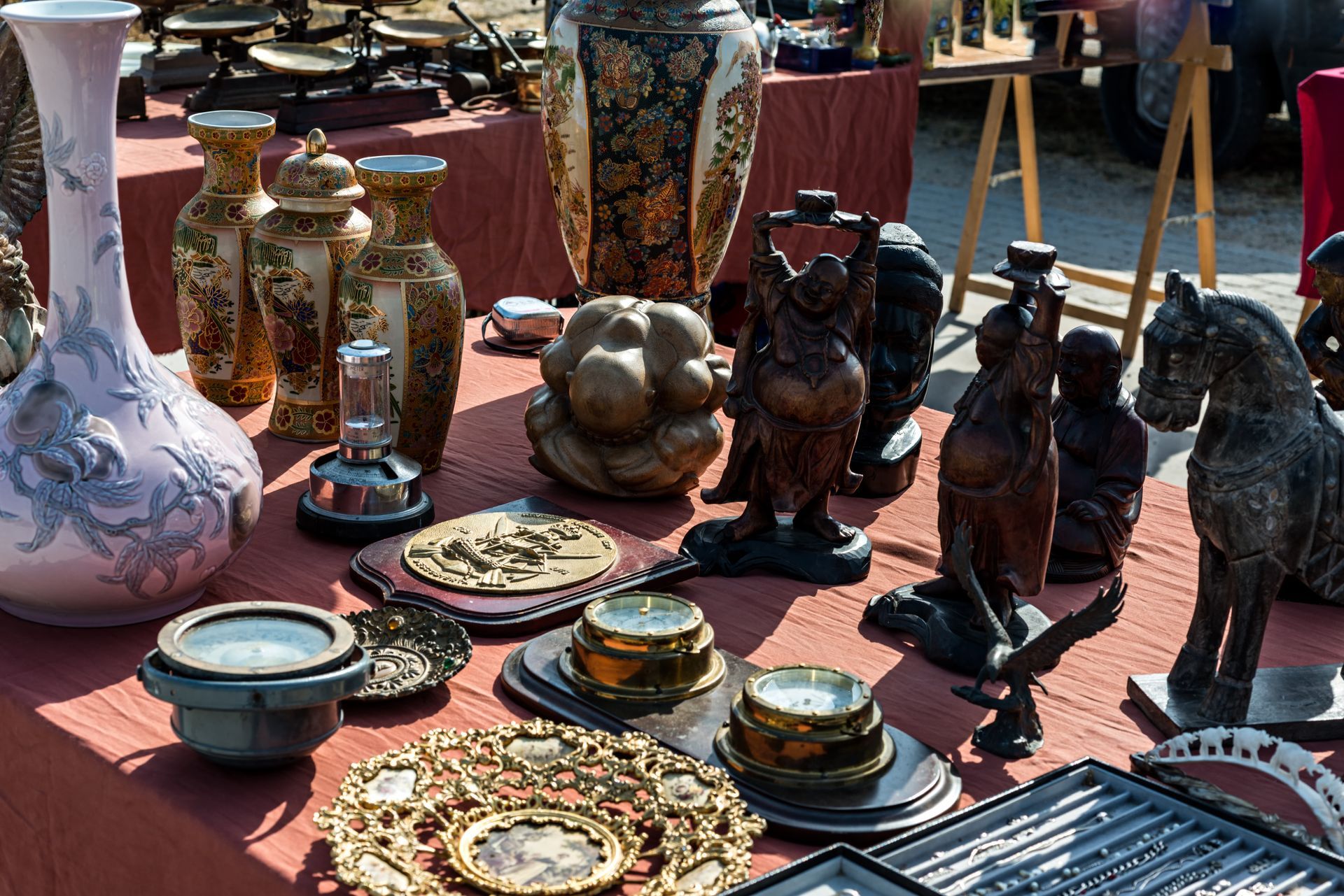 Table d'objets anciens sur un marché, comprenant vases, statues, bougies et assiettes décoratives.