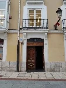 Fachada de un edificio beige con una puerta de madera, balcón y farola sobre una acera de piedra.