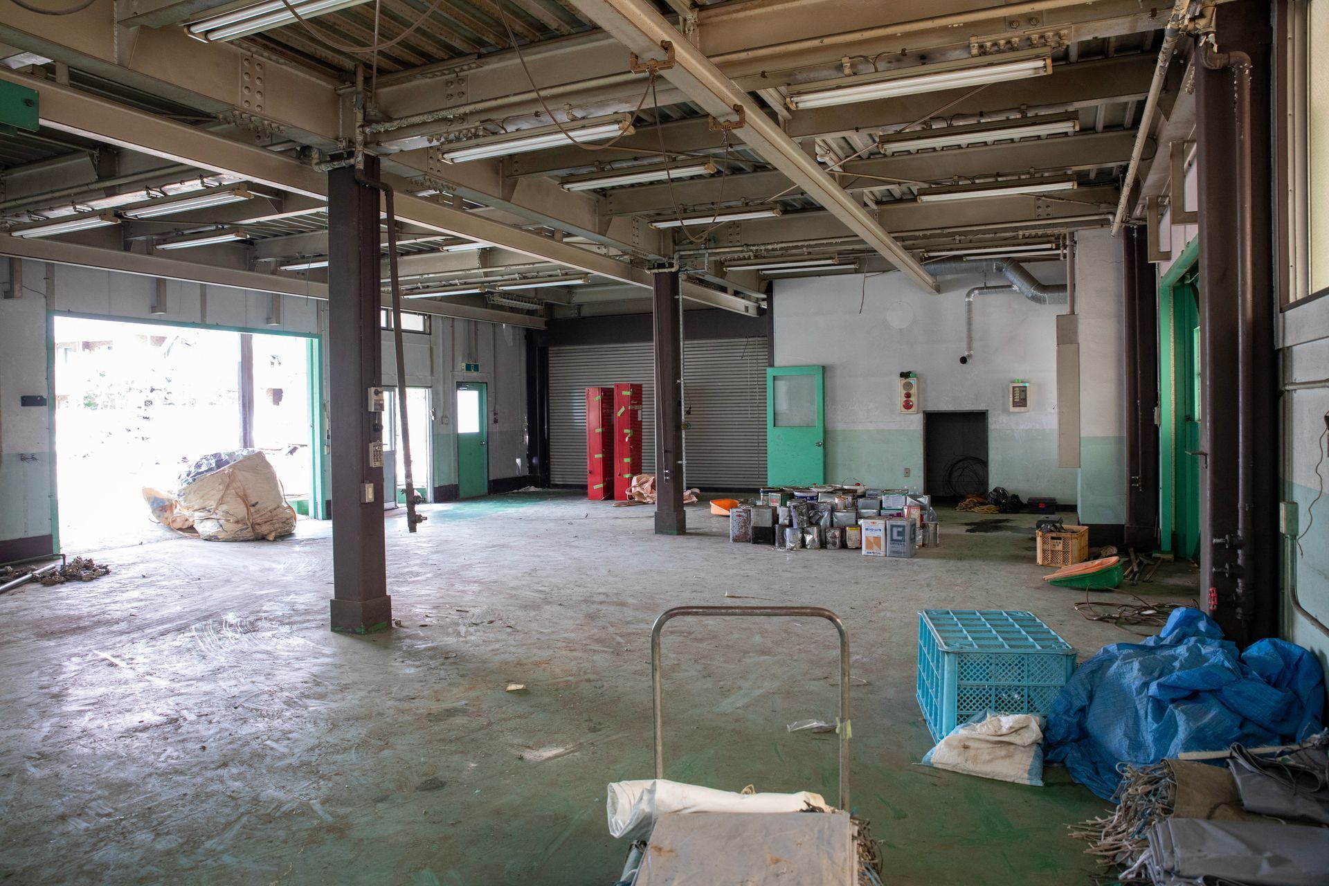 Un entrepôt industriel avec des plafonds apparents, des piliers de soutien, des fournitures éparpillées et des murs peints en vert.