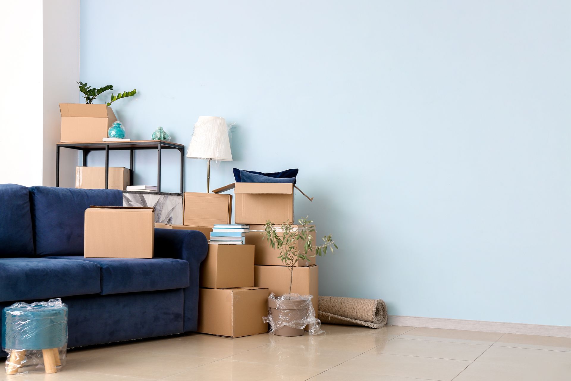Un canapé bleu à côté d'une étagère métallique et d'une pile de cartons dans une pièce aux murs bleu clair et au sol carrelé.