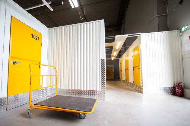Un chariot jaune à roulettes devant les portes jaunes d'un box de stockage, à l'intérieur d'un entrepôt de stockage propre.