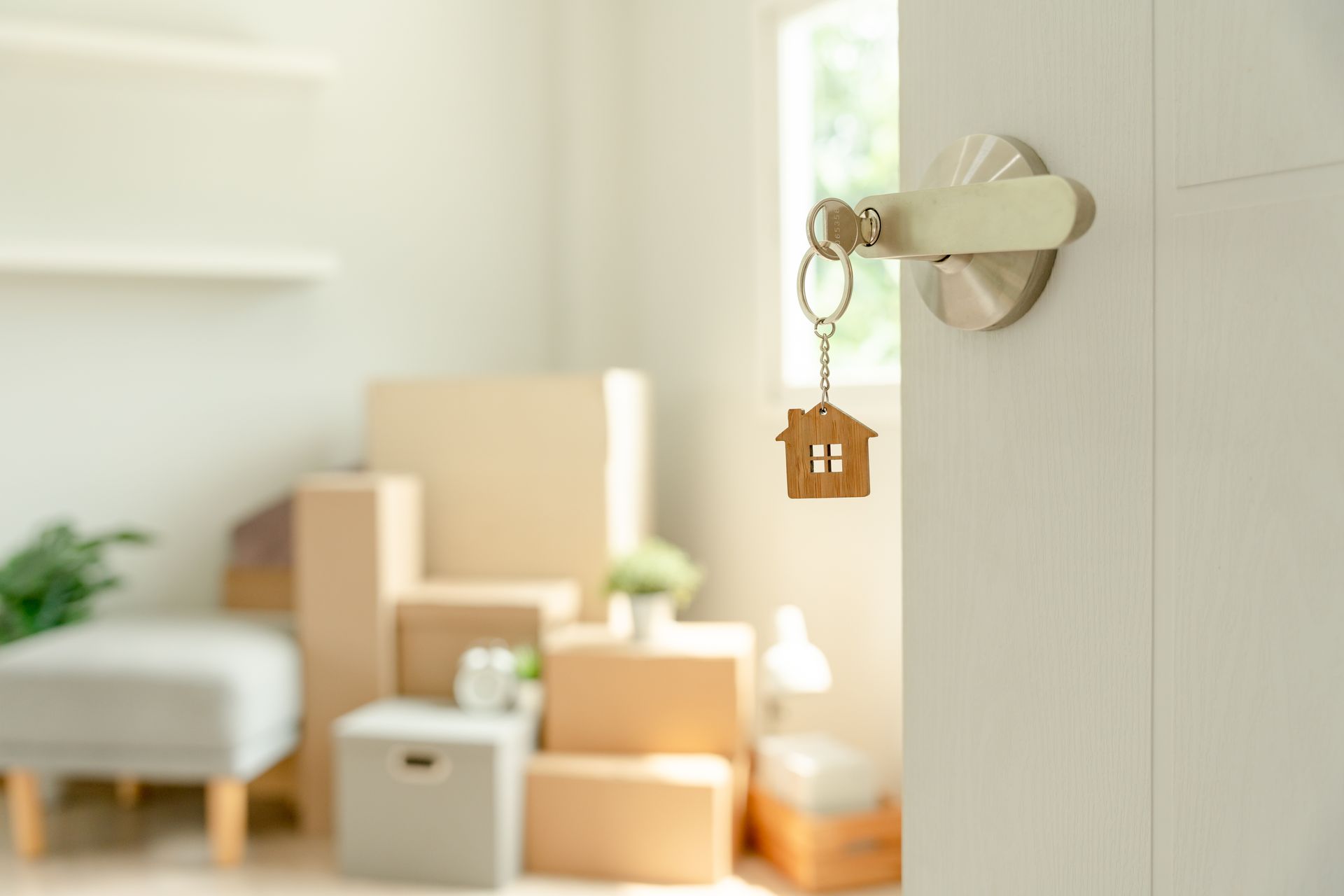 Un porte-clés en forme de maison accroché à une poignée de porte, avec des cartons de déménagement flous en arrière-plan.