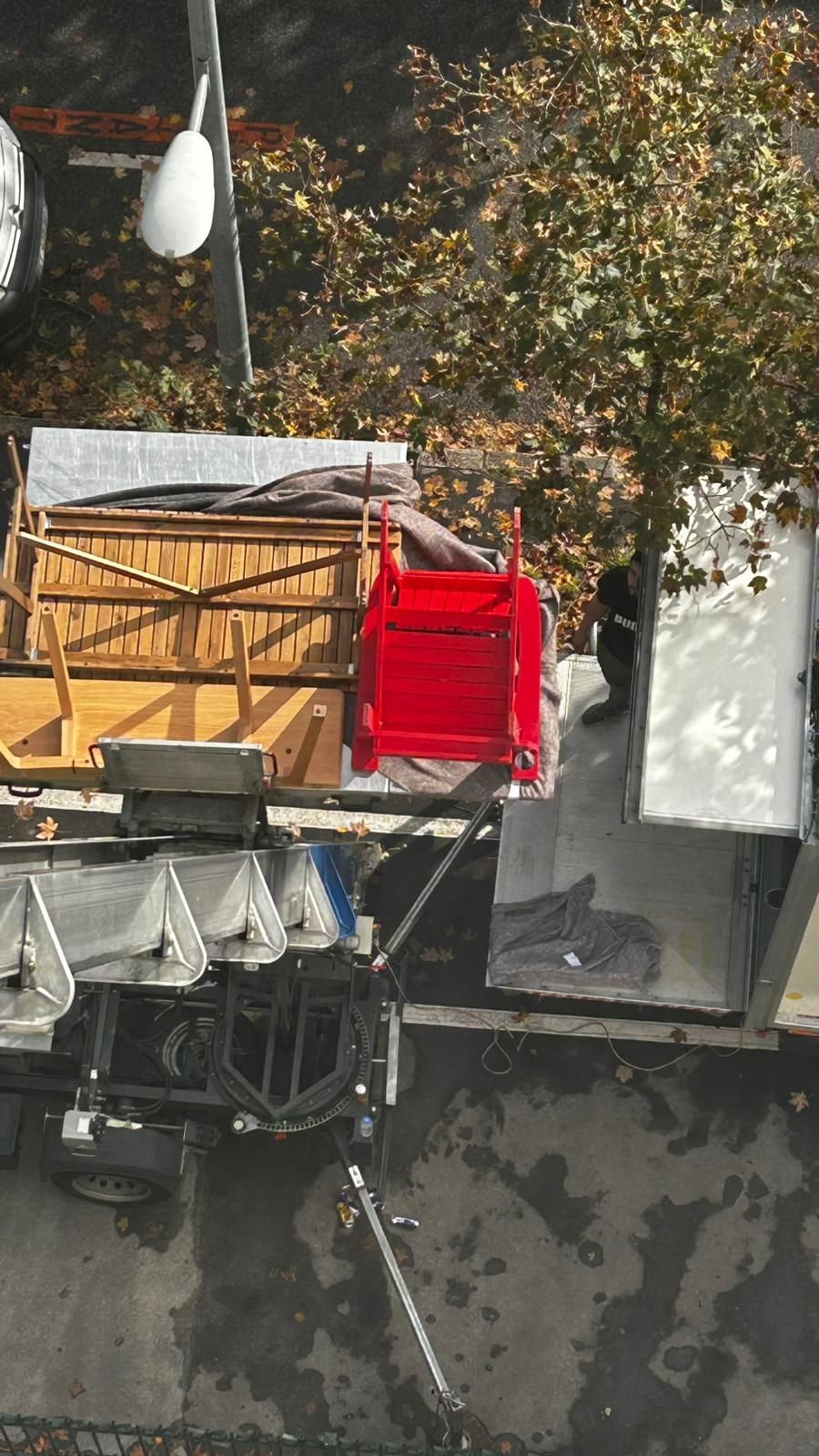 Une vue aérienne montre une table en bois, une chaise rouge vif et un plateau de table blanc chargés sur une remorque utilitaire à l'extérieur.