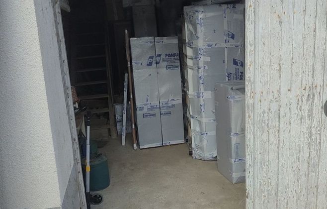 Vue à travers une porte donnant sur une zone de stockage contenant plusieurs grands paquets blancs rectangulaires emballés dans du plastique.