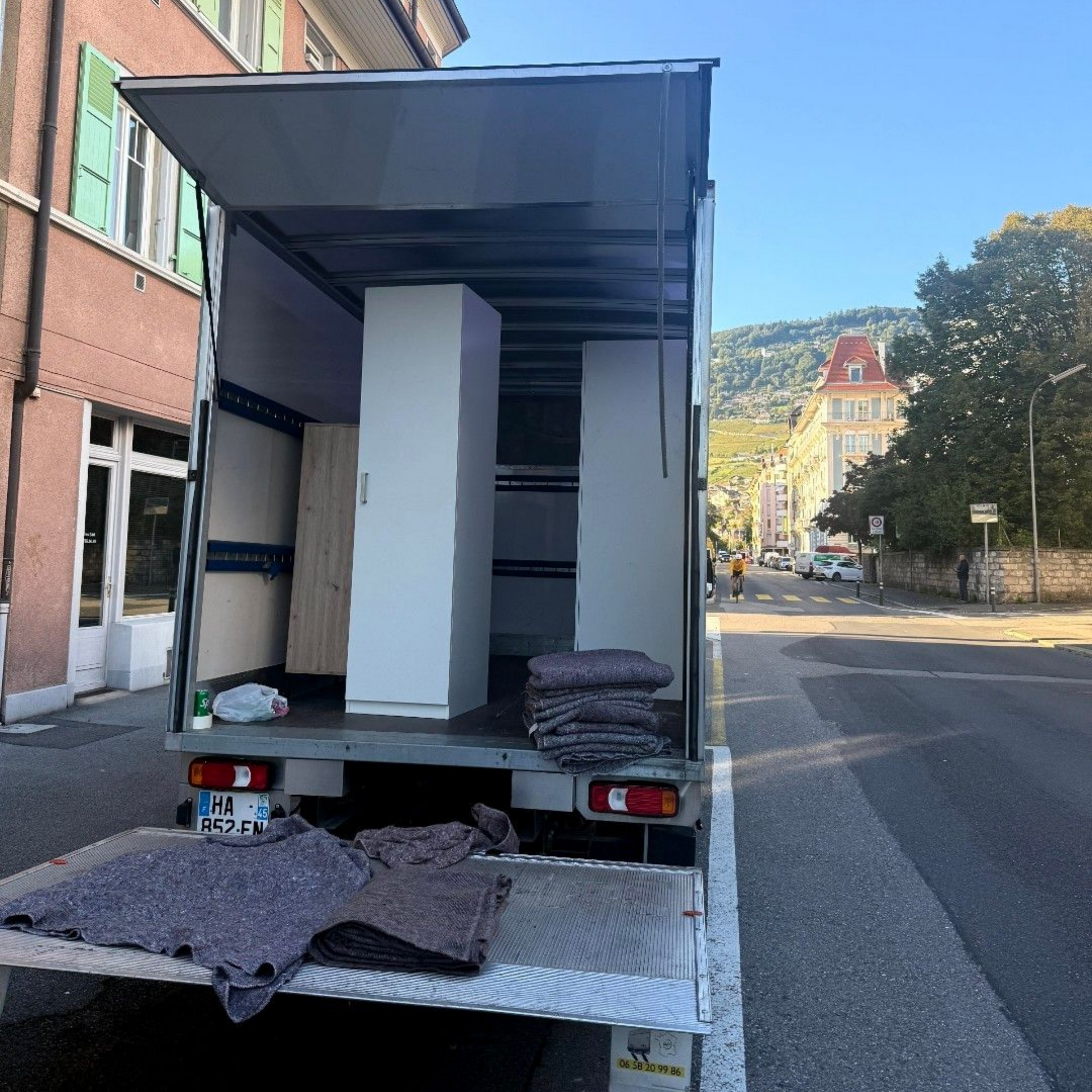 Un camion de déménagement stationné dans une rue de la ville contient deux armoires blanches et plusieurs couvertures de déménagement grises.