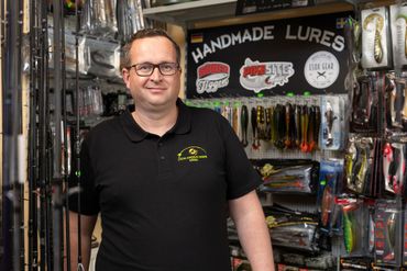 Ein Mann steht in einem Angelgeschäft vor einer Auslage mit Ködern.