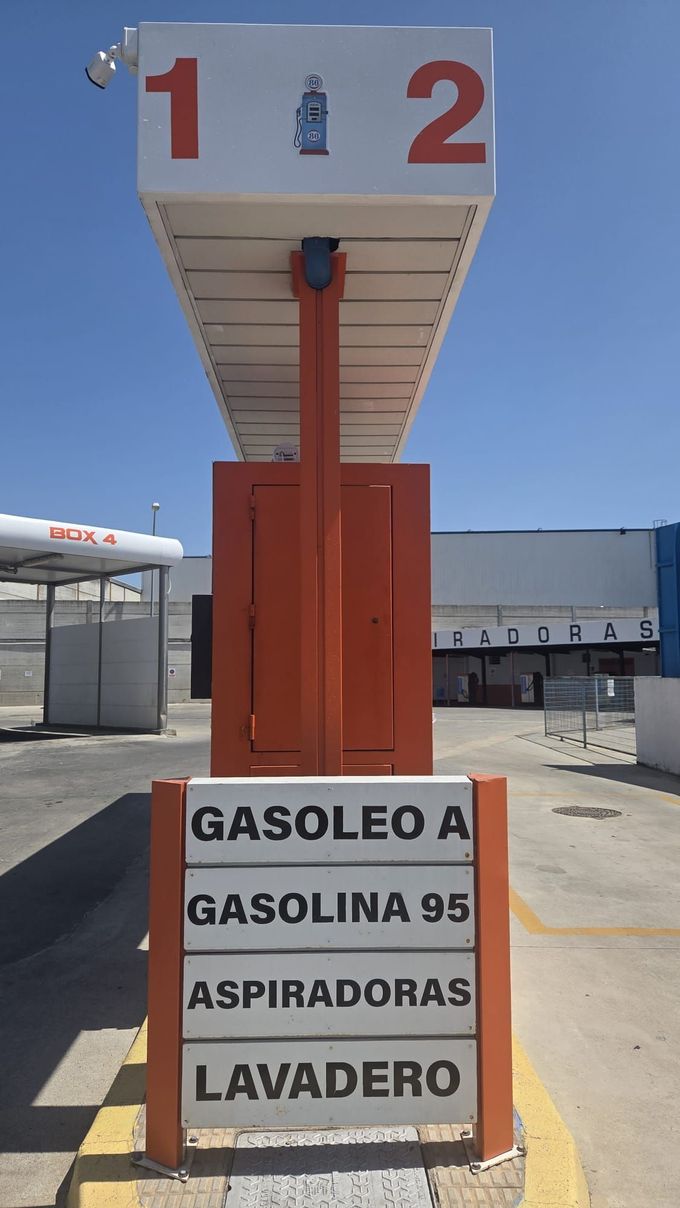 Surtidor de gasolina con toldo rojo marcado con los números 1 y 2, y letreros para diésel, gasolina 95, lavado de autos 