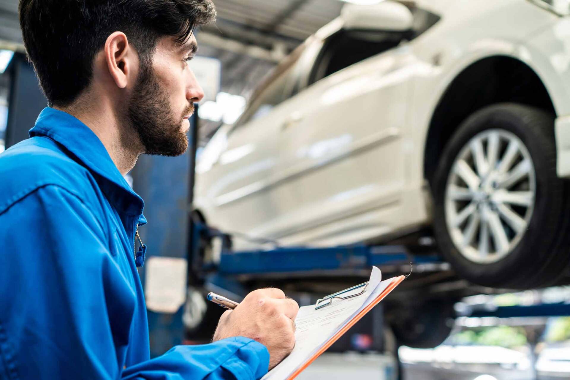 Mekaanikko kirjoittaa kirjoitusalustalle tarkastaessaan valkoista autoa.