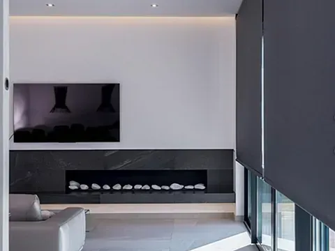 Sala de estar con chimenea oscura, TV y persianas enrollables grises.