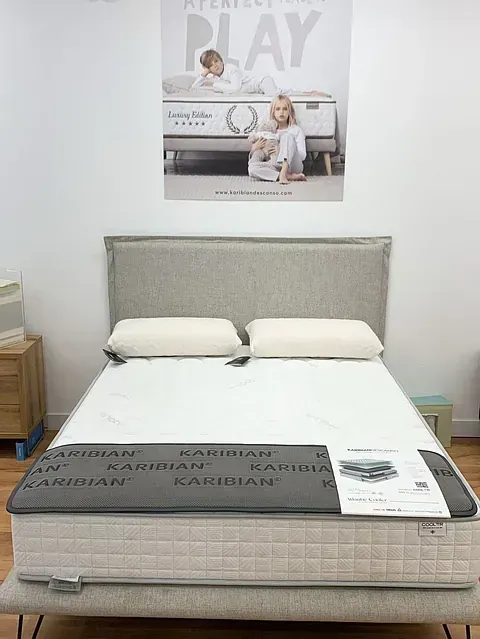 Colchón con almohadas y cabecero en exposición, bajo un cartel de