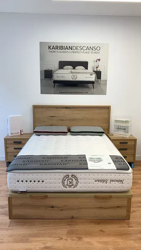 Exhibición de dormitorio con estructura de cama de madera, colchón, cabecero, mesitas de noche y publicidad.