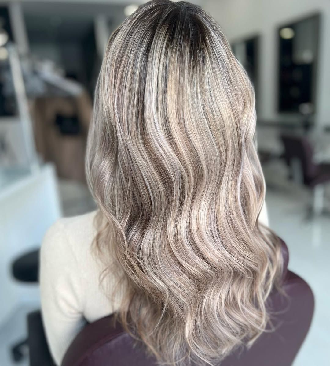 Una mujer con cabello largo y rubio está sentada en una silla en un salón.