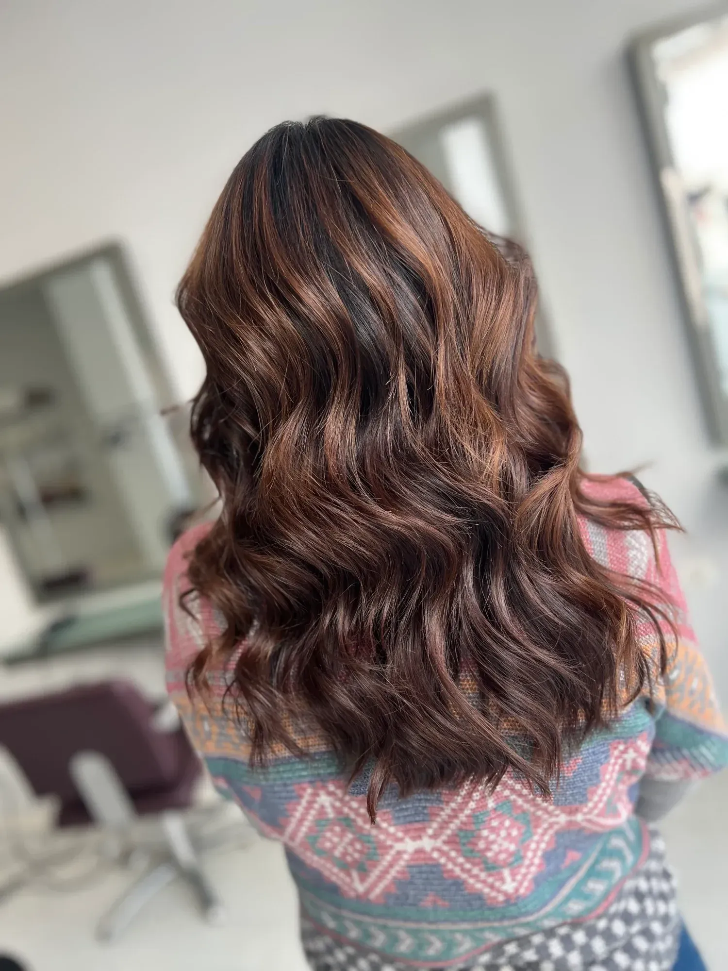 Una mujer con cabello largo y castaño está sentada en una silla en un salón.