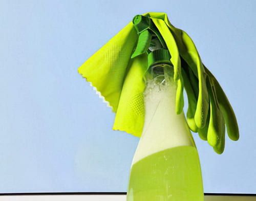 Una botella de spray con un paño verde y guantes encima.