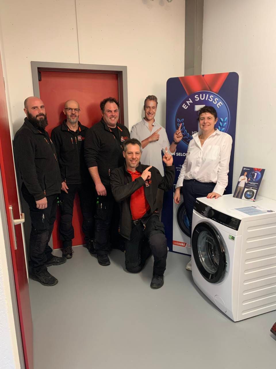 Equipe à côté d'une machine à laver à chargement frontal et d'une banderole publicitaire bleue et rouge dans un couloir