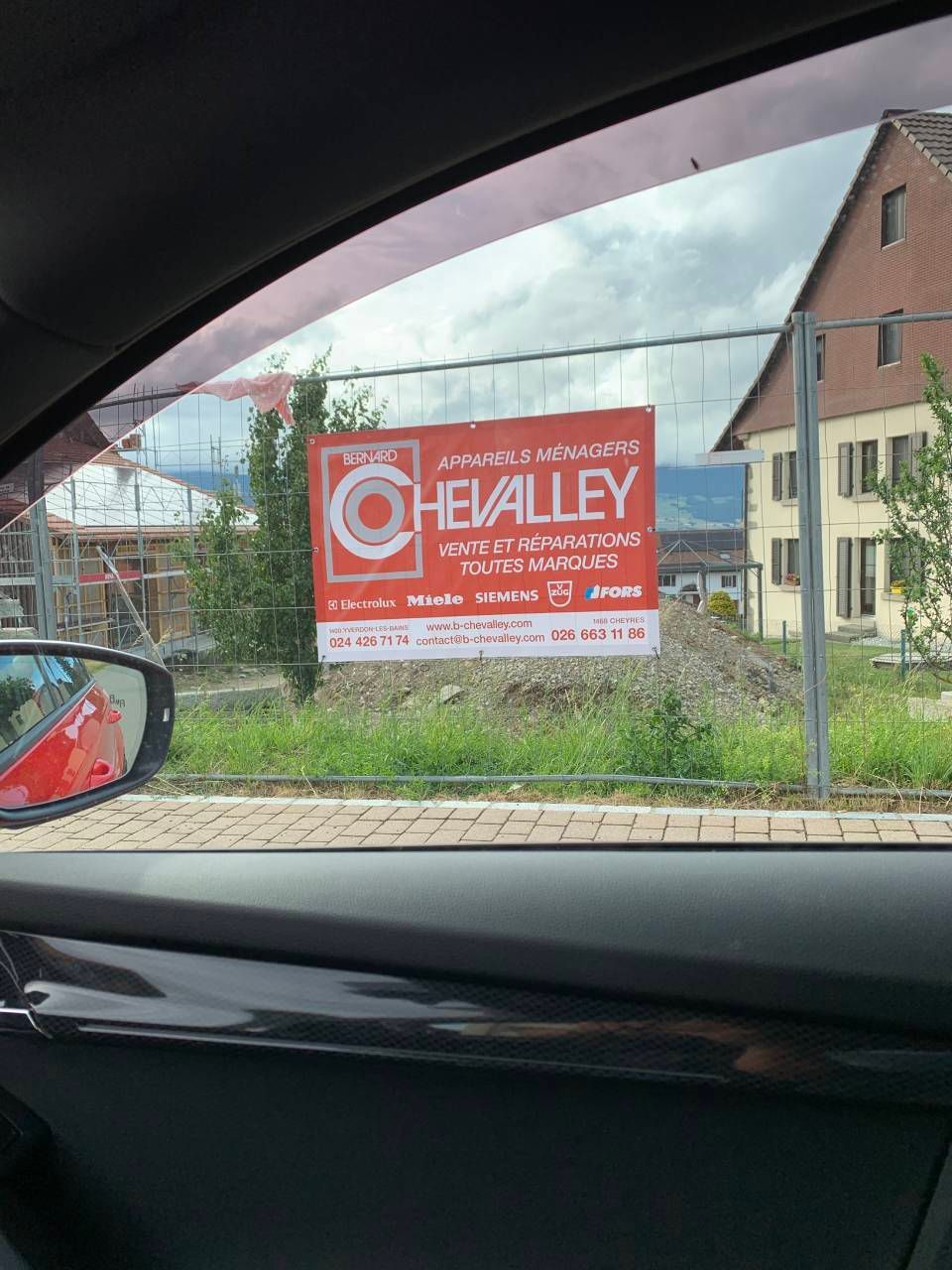 Vue depuis une voiture d'un panneau publicitaire rouge pour des logements de la marque Chevalley, en bord de route.