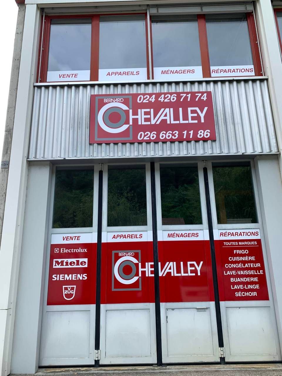 Façade du magasin Chevalley avec enseigne rouge, numéros de téléphone et portes/fenêtres vitrées sur un bâtiment commercial