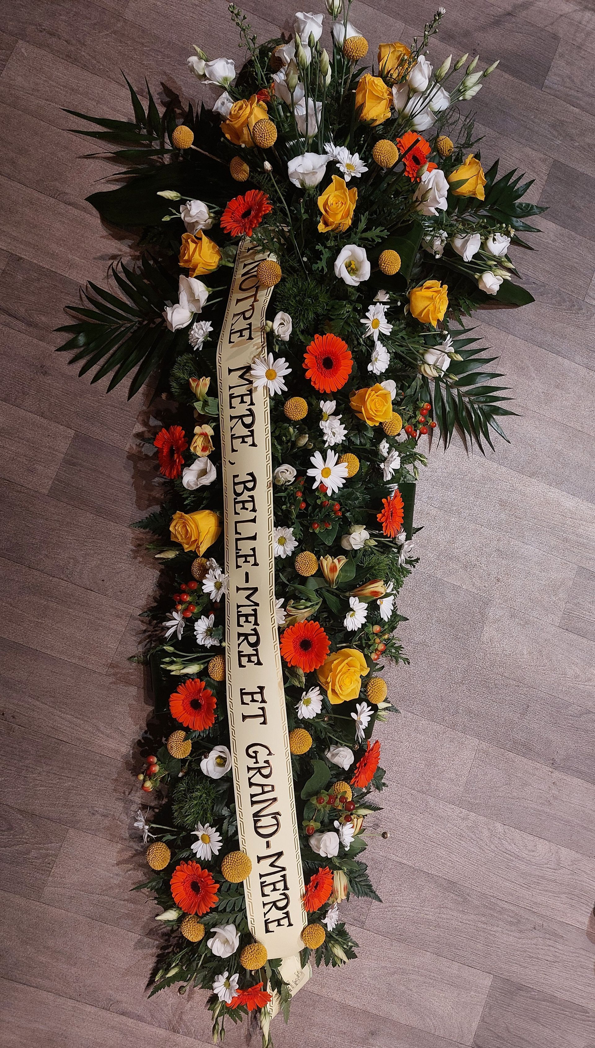 Composition florale avec des fleurs rouges, jaunes et blanches, et un ruban portant une inscription.