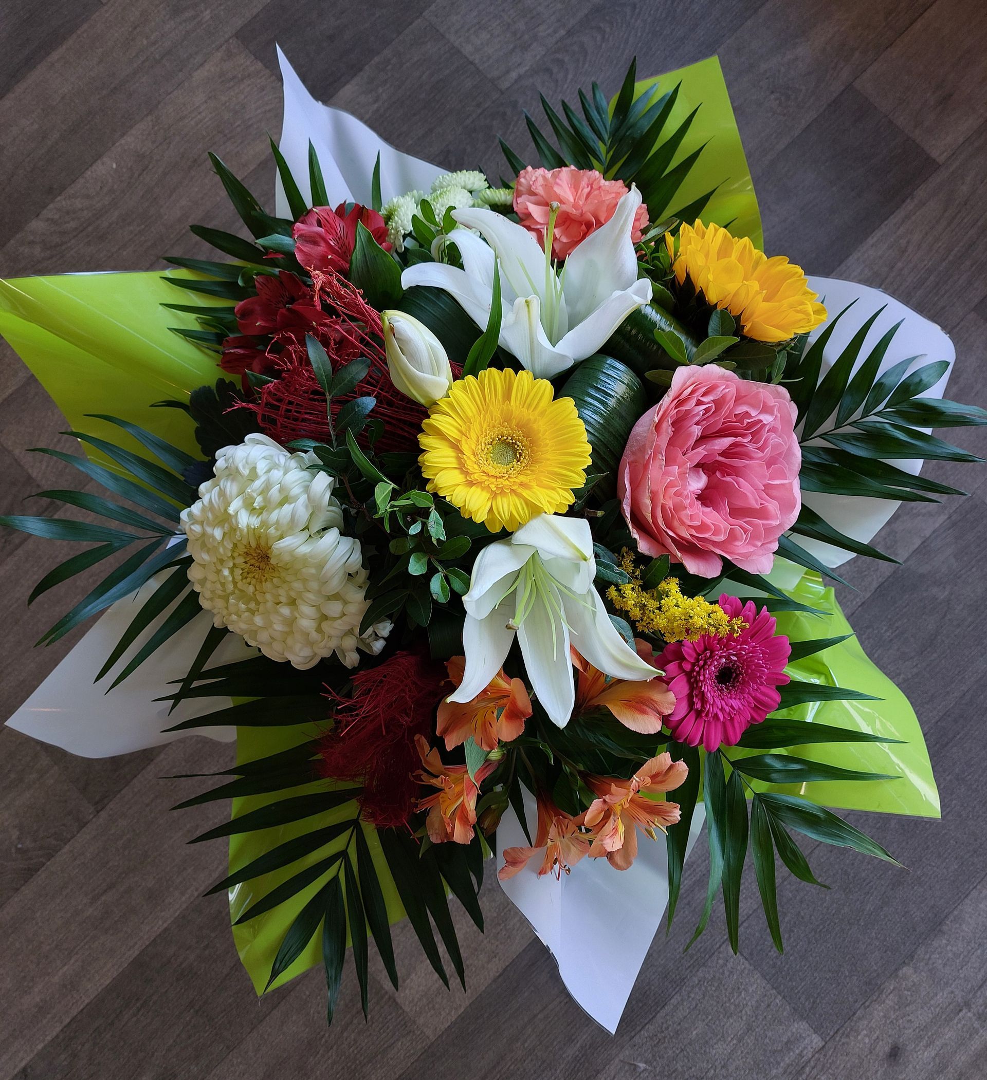 Bouquet coloré de fleurs, comprenant des lys, des gerberas et des œillets, enveloppé dans du papier blanc et vert citron