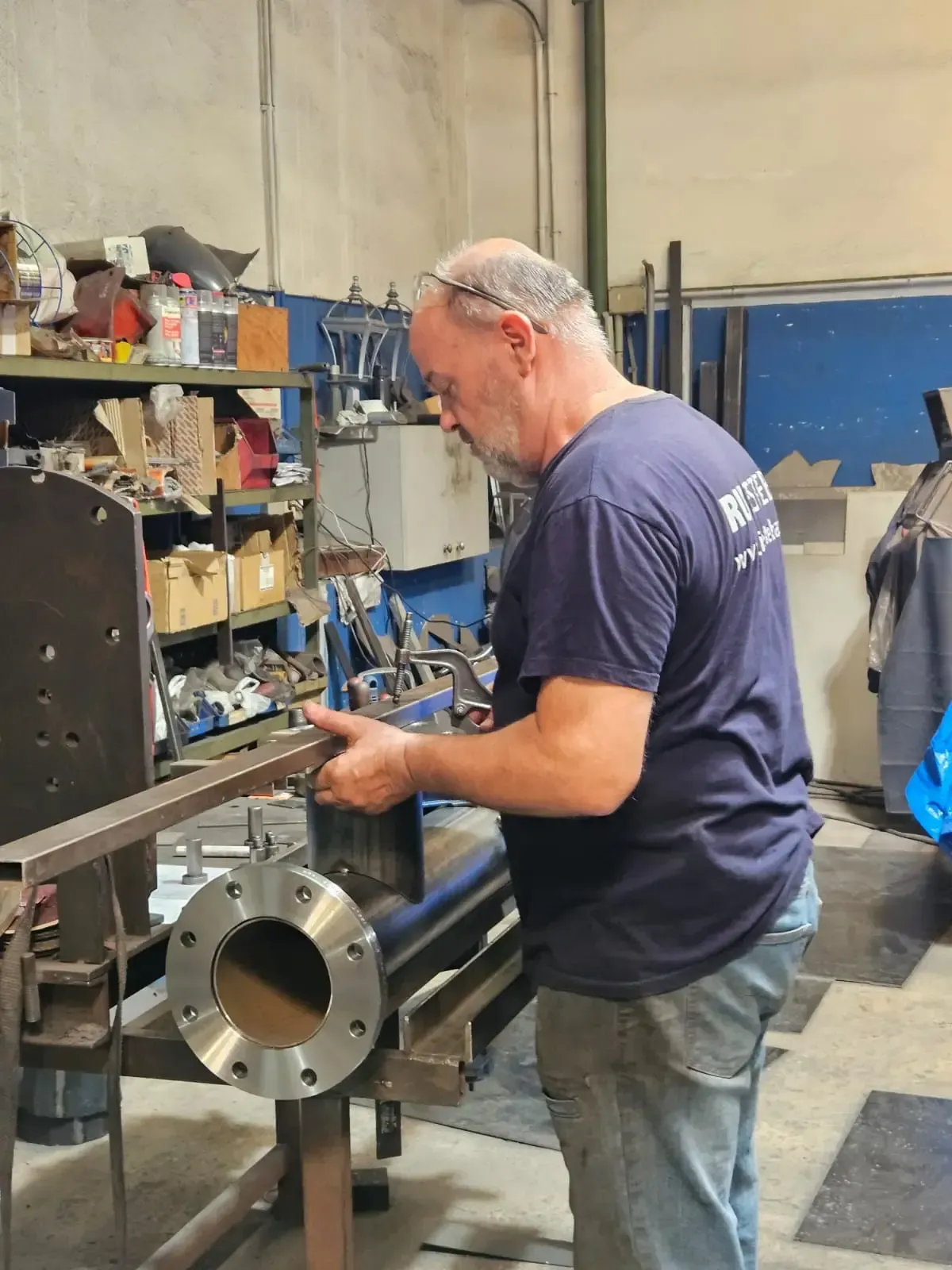 Técnico con mono azul trabajando en una brida de tubería metálica grande en un entorno industrial.
