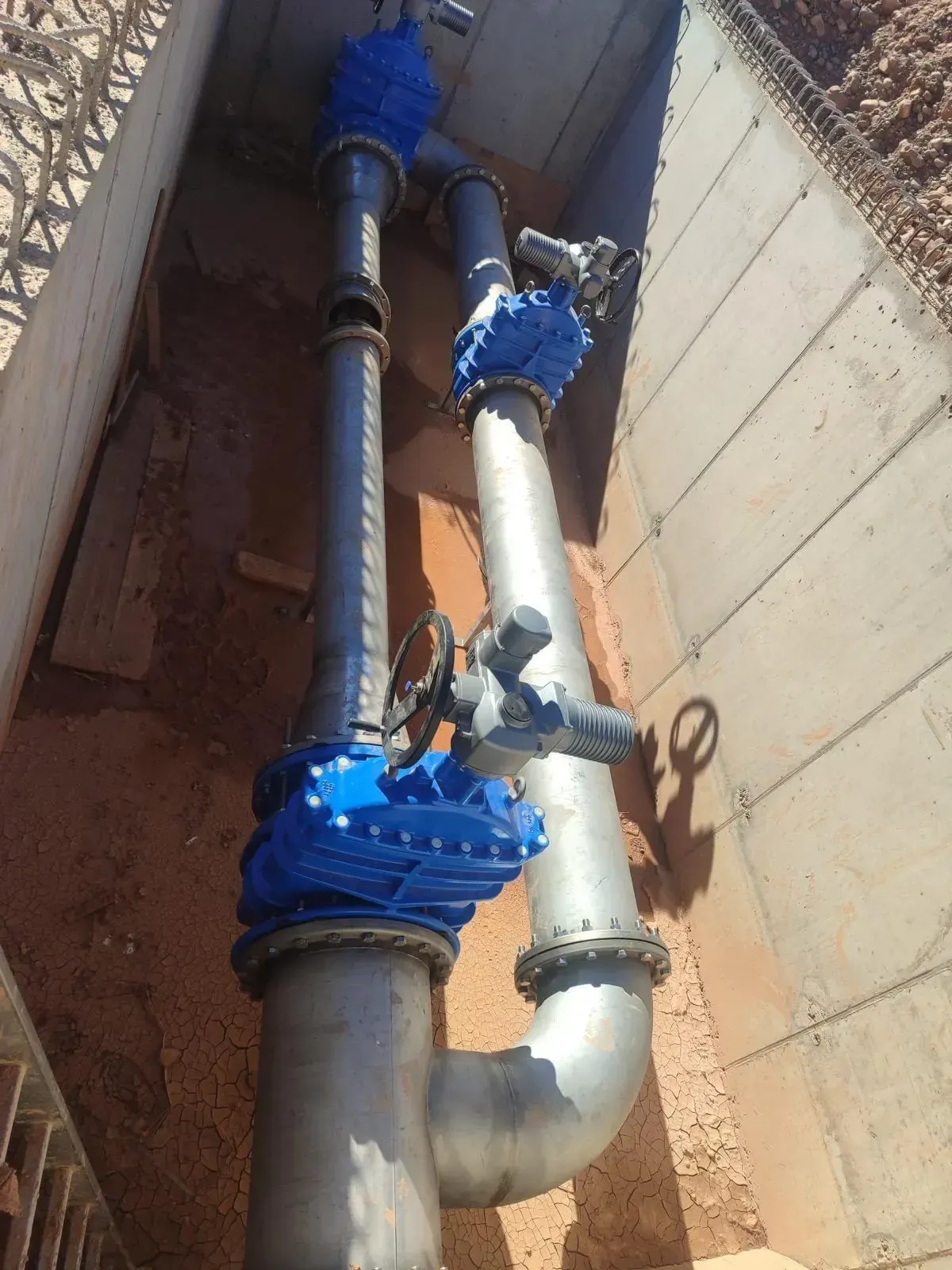 Tuberías verticales con válvulas azules en un estrecho conducto de servicios.