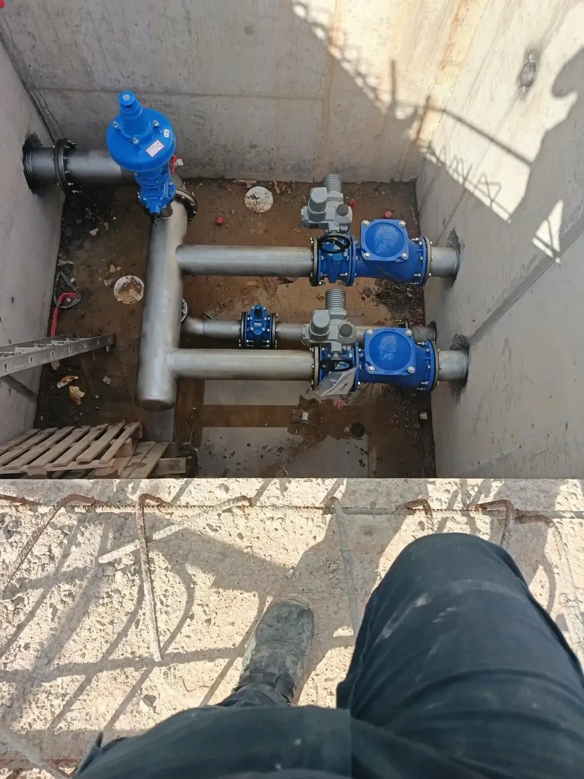 Tuberías de servicios públicos y válvulas azules en una fosa de servicio de hormigón, vistas desde arriba.