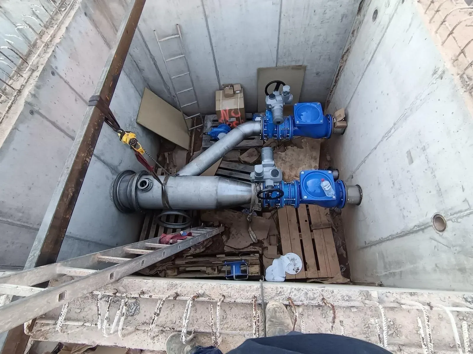 Los trabajadores inspeccionan bombas y tuberías industriales azules dentro de un pozo de hormigón para servicios públicos.