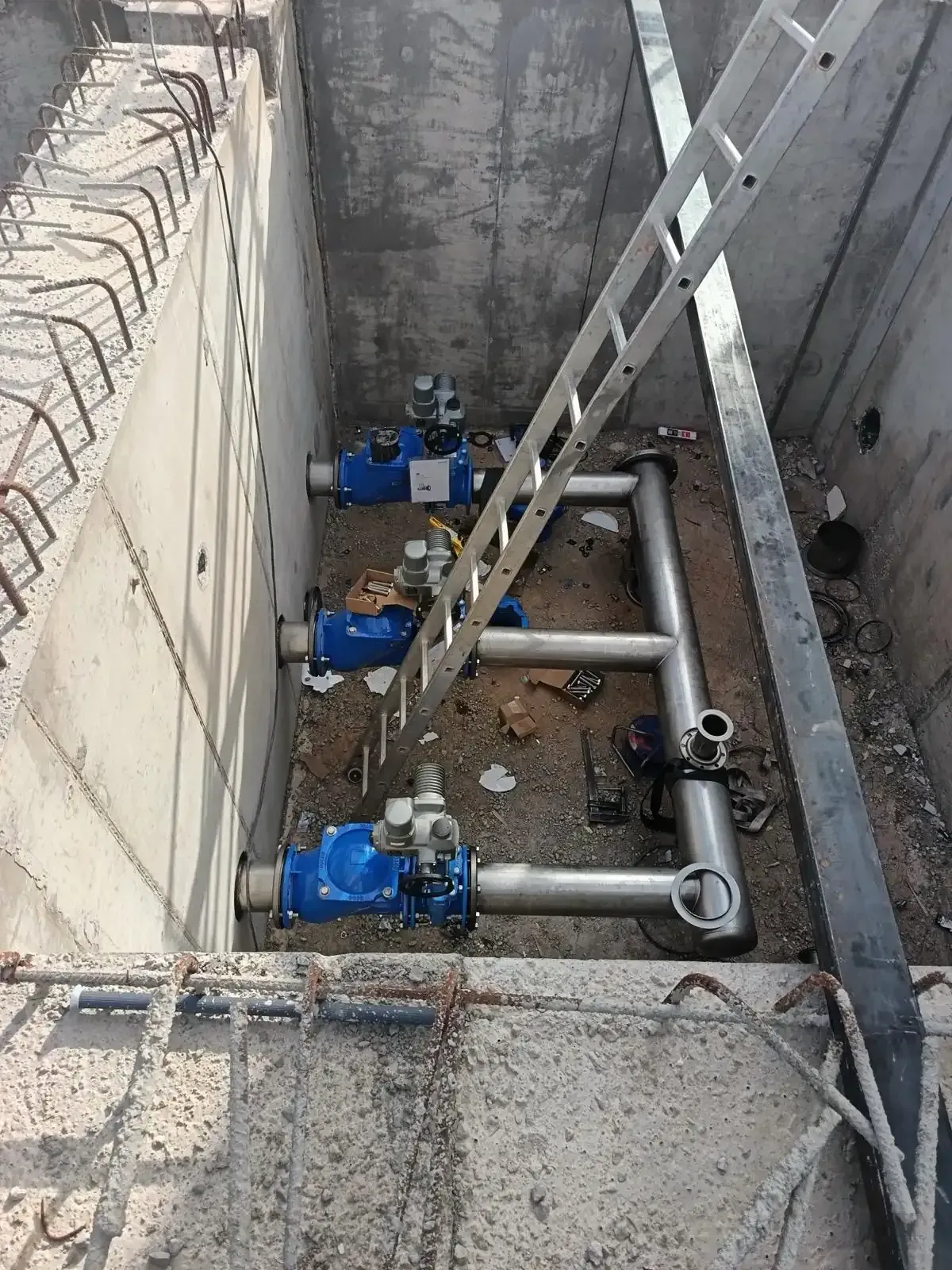 Foso industrial con tres bombas azules y tuberías plateadas junto a una pared de hormigón
