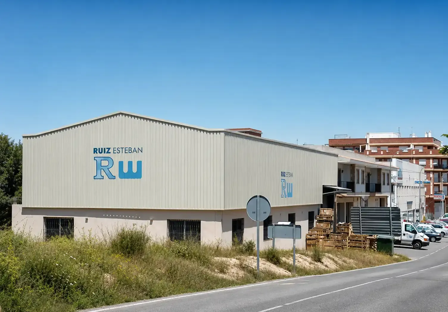 Edificio industrial bajo con el logotipo de RW junto a una carretera bajo un cielo azul despejado.