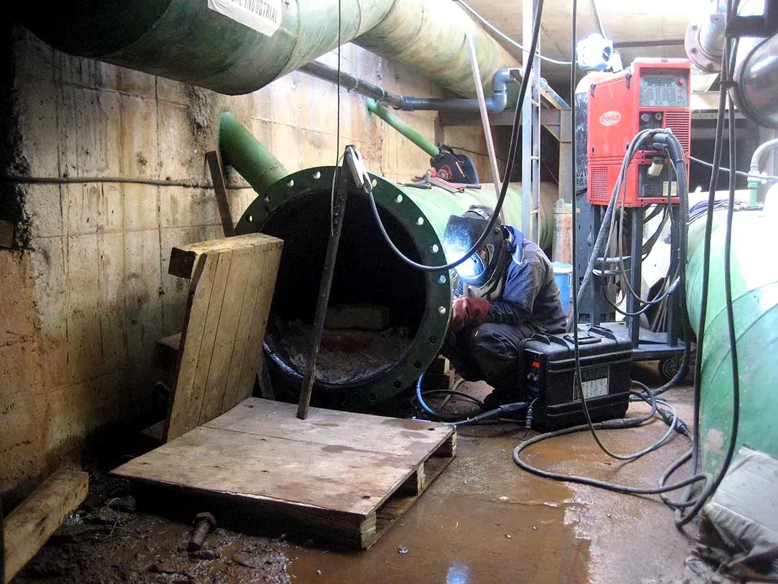 Trabajador dentro de una tubería de alcantarillado utilizando una herramienta de soldadura en una zona de