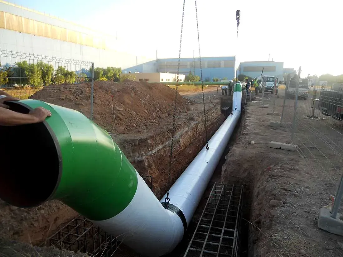 Se está instalando una gran tubería de color verde y blanco en una zanja de construcción al aire libre.
