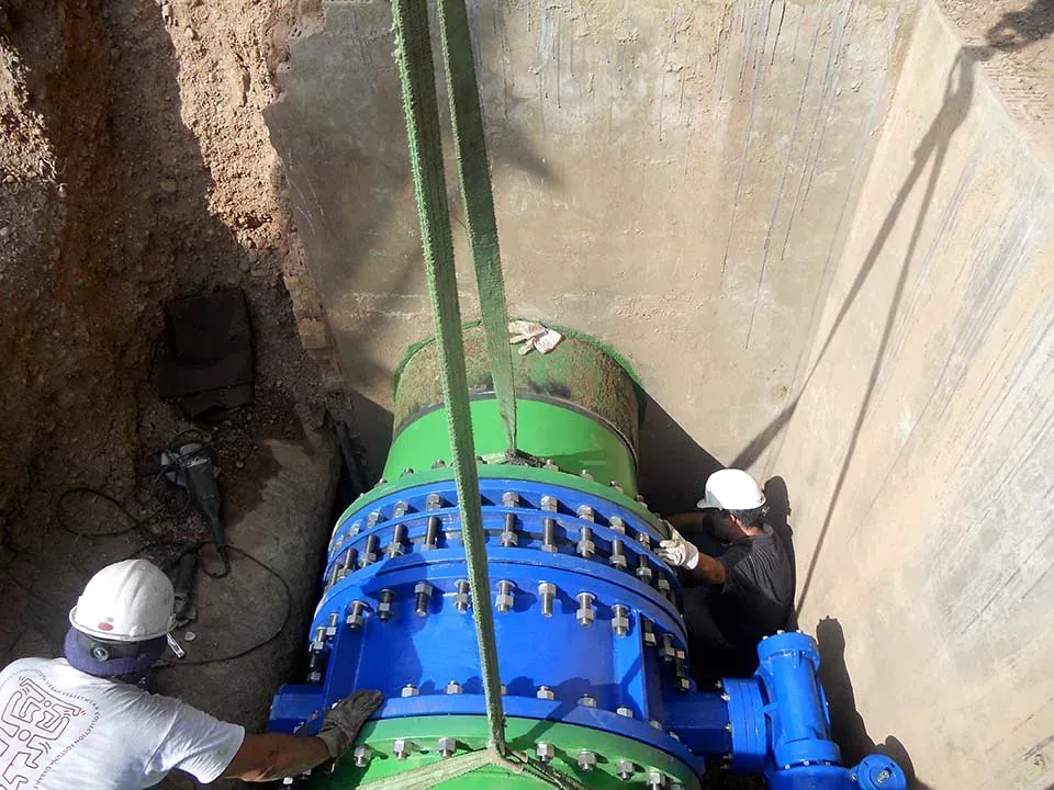 Trabajadores instalando un gran tramo de tubería azul y verde en una zanja.