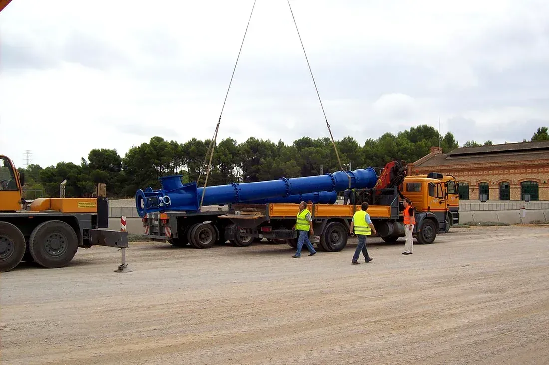 Trabajadores junto a una pesada máquina azul sobre un camión en un depósito de grava