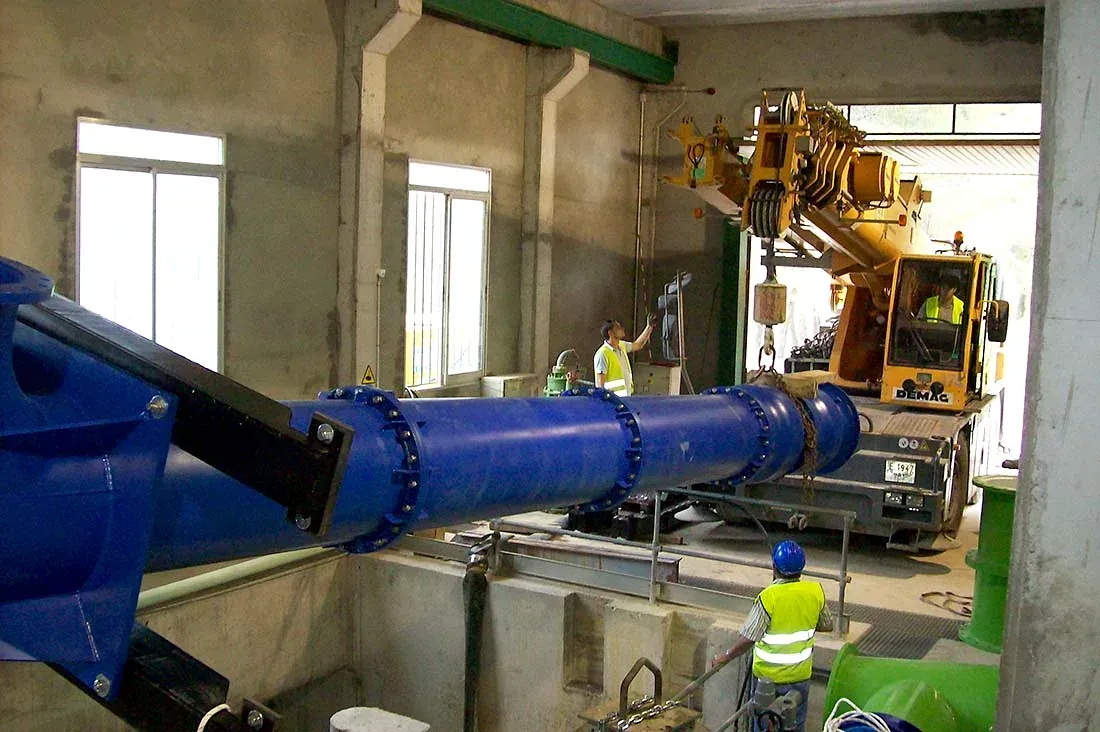Tubería industrial azul en una fábrica, con maquinaria pesada y un trabajador con casco cerca.