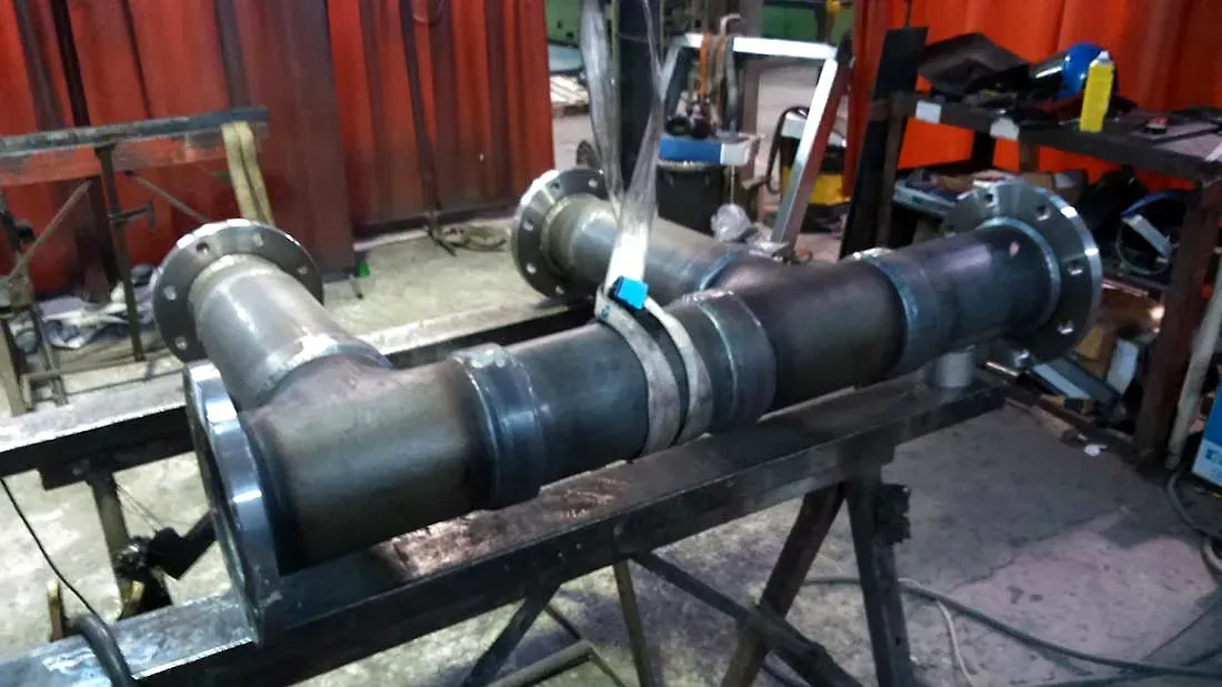 Gran conjunto de tuberías de metal negro sobre el suelo de un taller, con abrazaderas y maquinaria al fondo.
