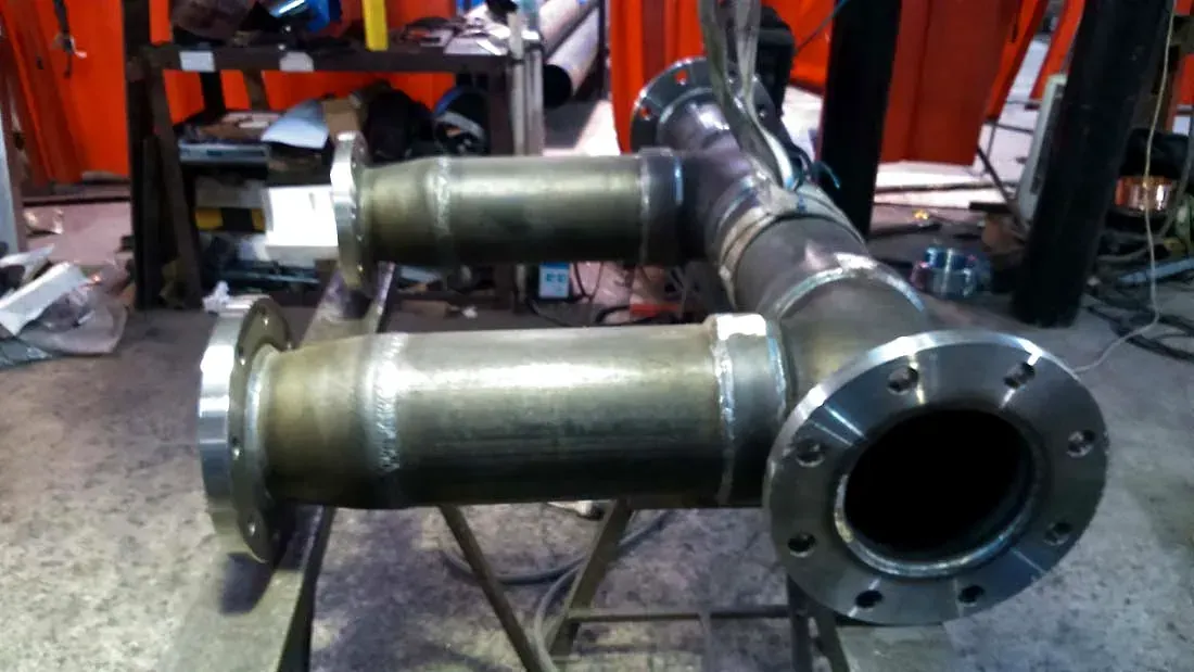 Tubos metálicos industriales con extremos bridados dispuestos en el suelo de un taller.
