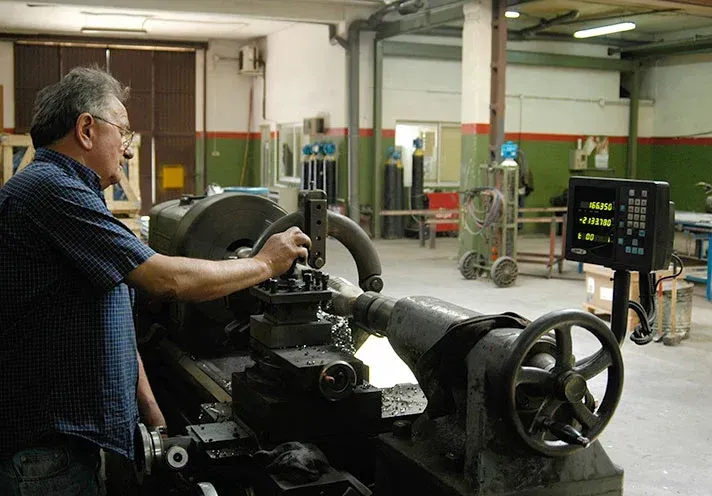 Hombre manejando un gran torno de metal en un taller industrial.