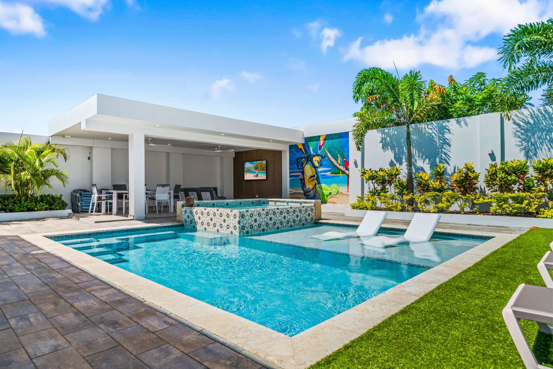 Modern backyard with a blue swimming pool, white lounge chairs, patio, and tropical landscaping