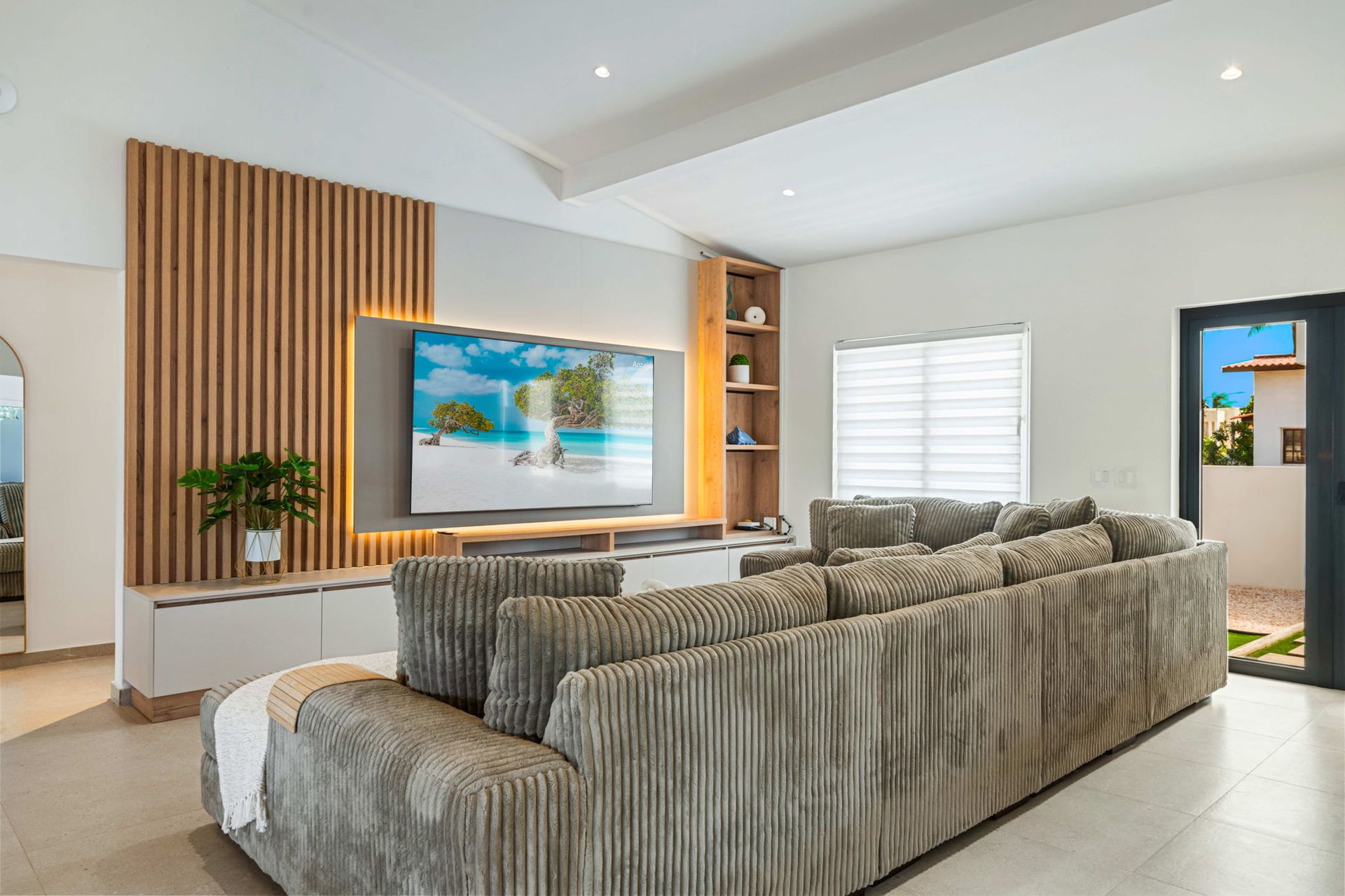 Modern living room with gray sectional sofa, wood slat accent wall, TV, and bright windows