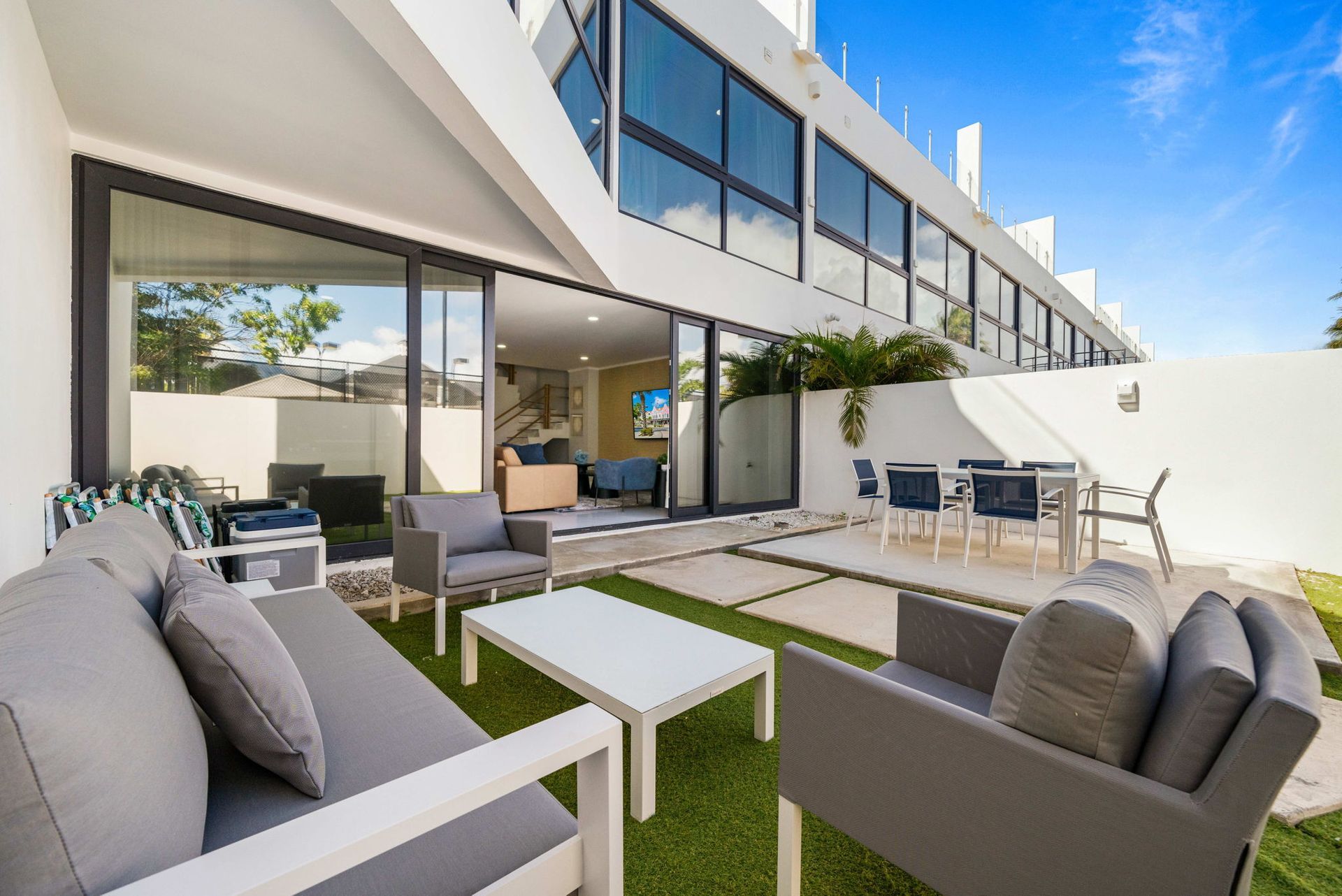 Modern patio with gray seating, white tables, and sliding glass doors beside a contemporary home