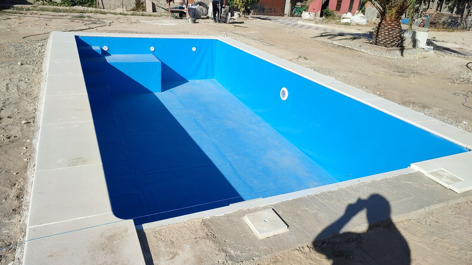Se está construyendo una gran piscina azul en un campo de tierra.