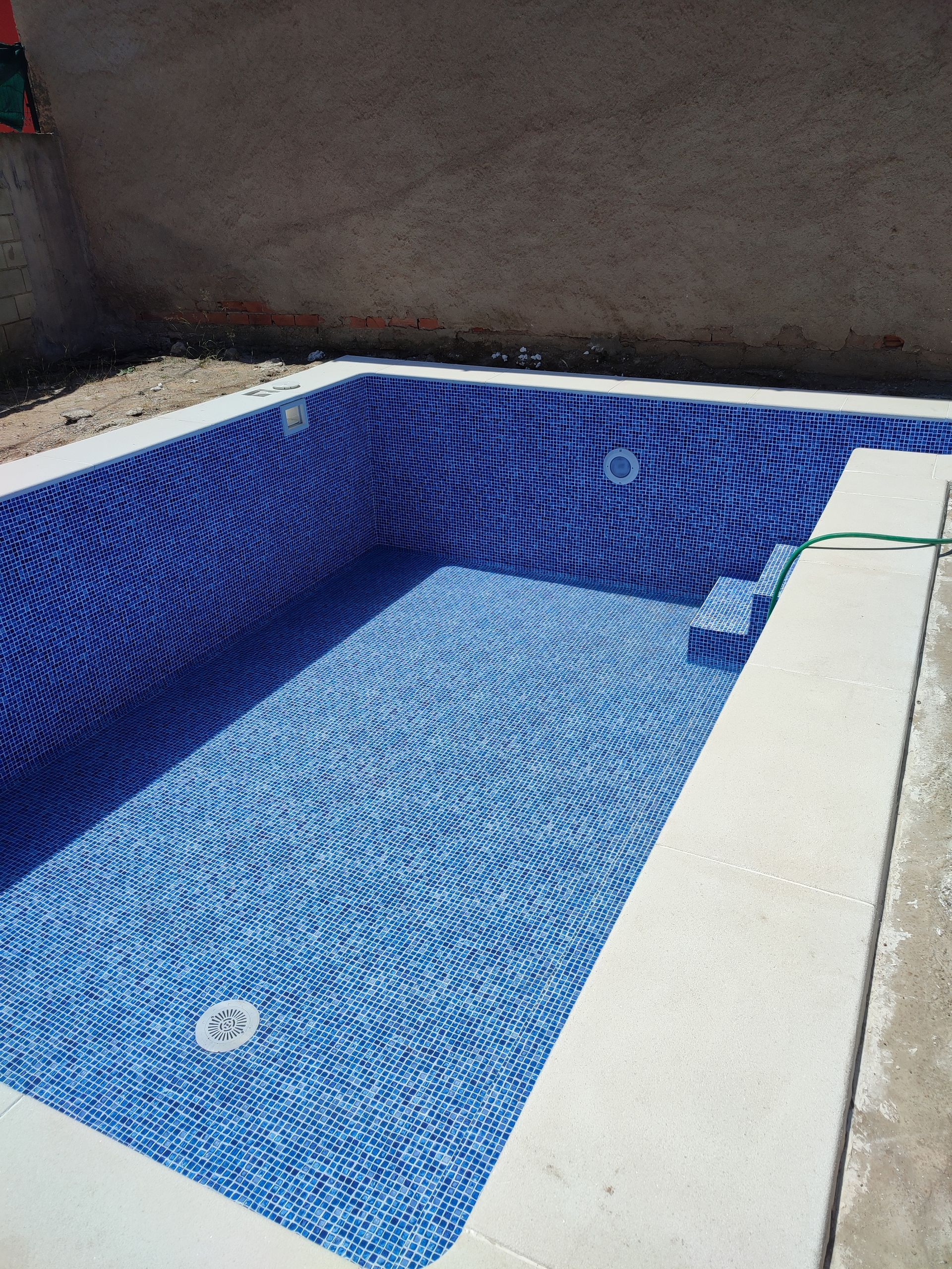 Se está construyendo una piscina con azulejos azules y borde blanco.