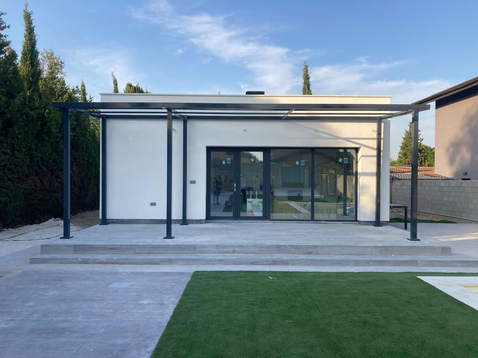 Una pequeña casa blanca con pérgola y puertas corredizas de vidrio.