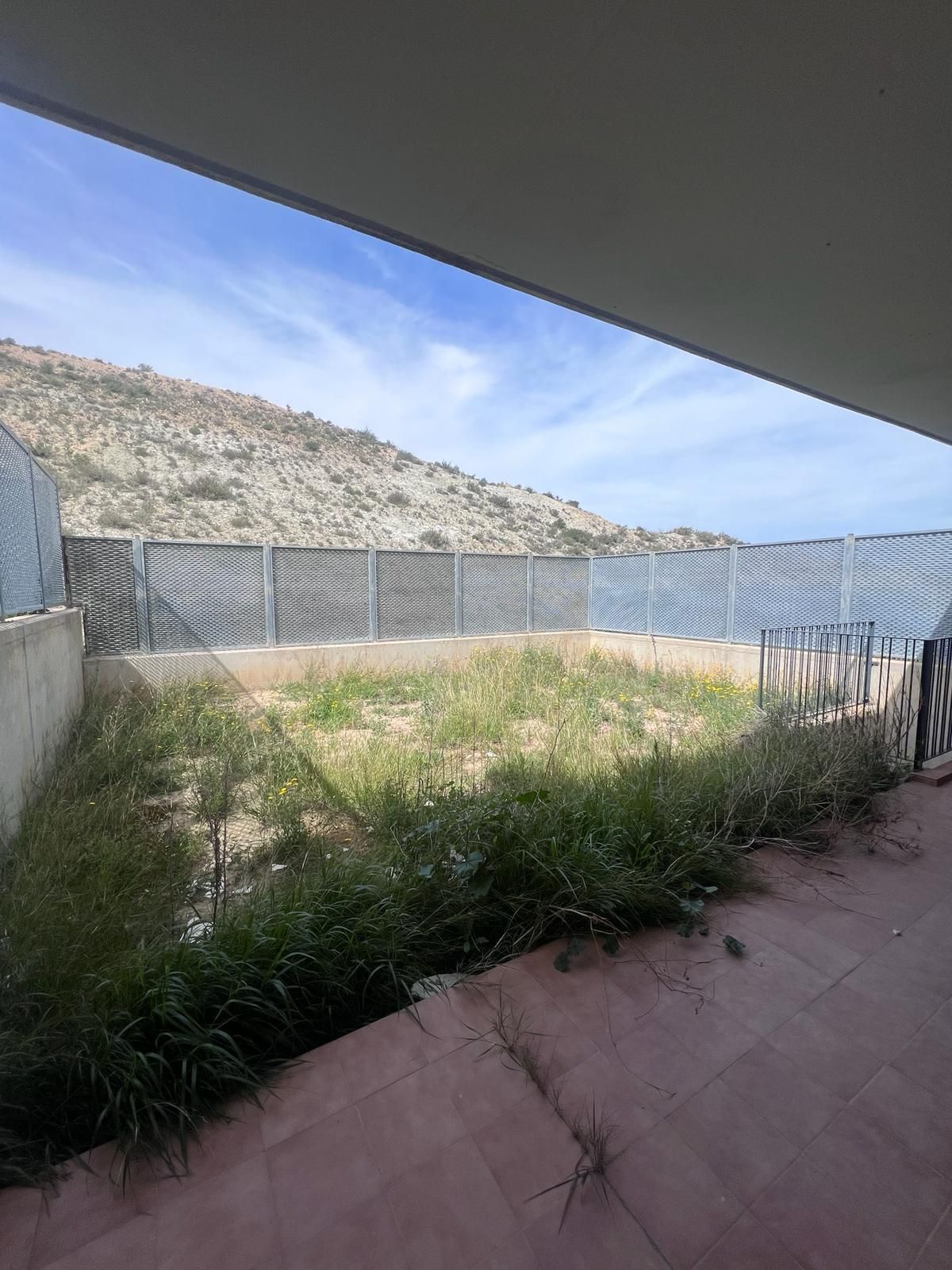 Un patio cercado con mucho césped y una montaña al fondo.