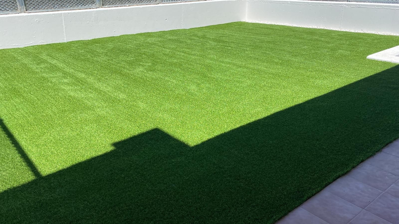 Un césped verde exuberante con una valla blanca al fondo.