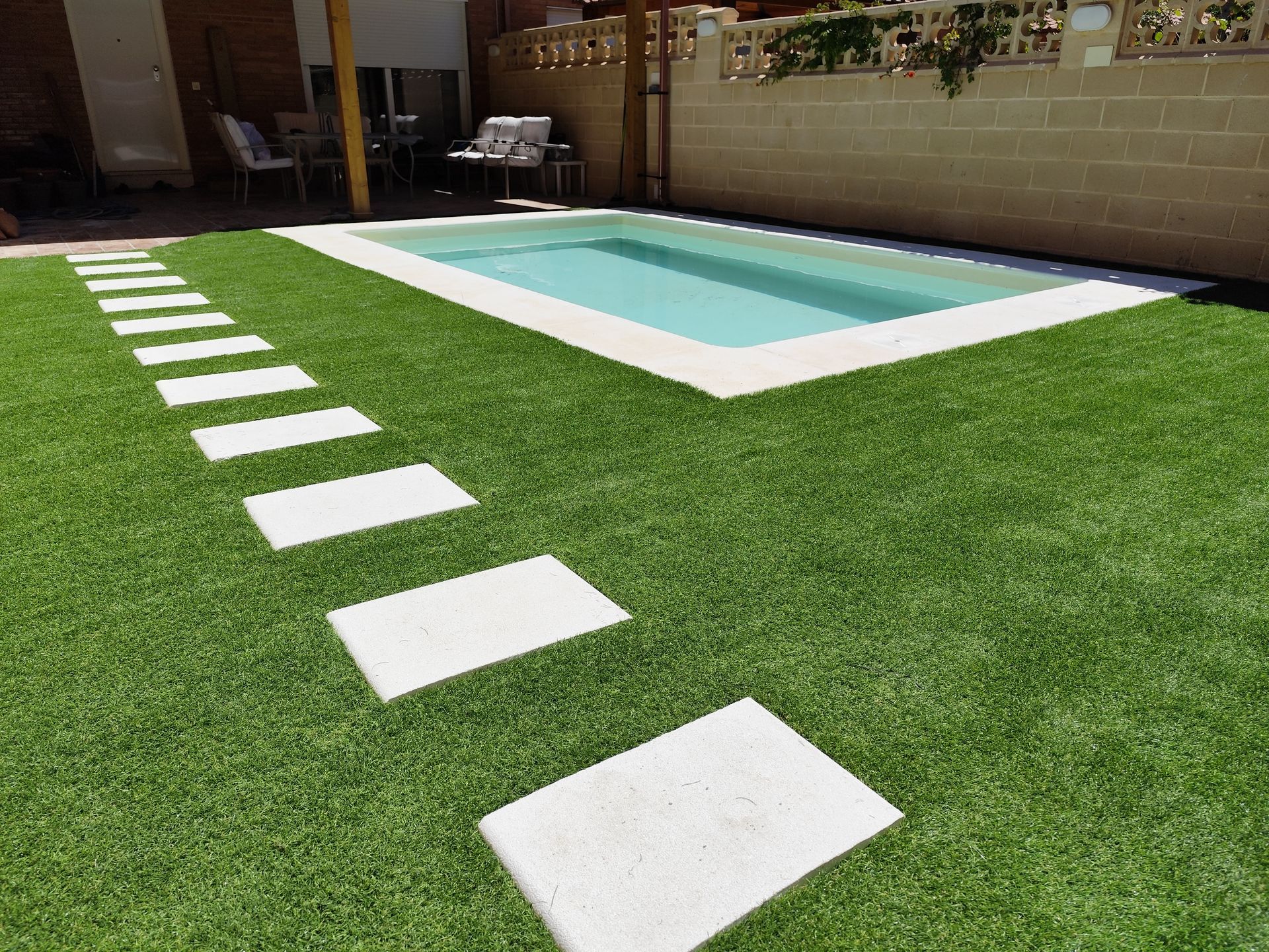 Una piscina está rodeada de un exuberante césped verde y escalones de piedra blancos.
