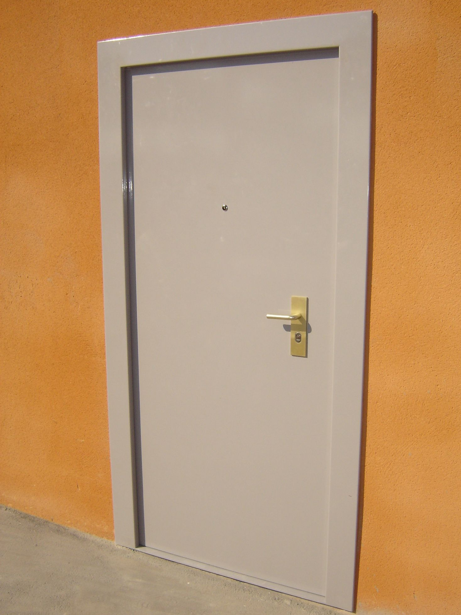 Porte grise avec poignée dorée et judas dans un cadre mural orange.